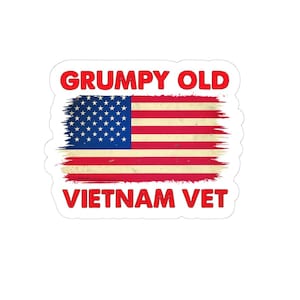 May include: A sticker featuring the American flag with a distressed design. The words "GRUMPY OLD" are above the flag, and "VIETNAM VET" is below, all in red text.