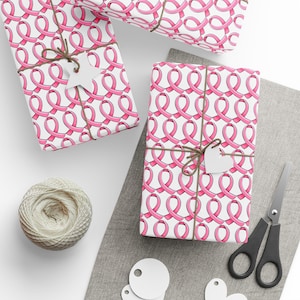 May include: Three white gift boxes wrapped in pink ribbon patterned paper. The boxes are tied with brown twine and have white gift tags attached.