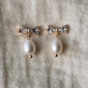 A pair of pearl drop earrings with crystal accents, displayed on a textured fabric background.