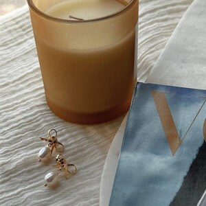 Earrings laid next to a candle and Vogue magazine. An aesthetic lifestyle setup that evokes calm luxury and giftable appeal.