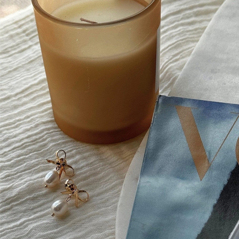 Earrings laid next to a candle and Vogue magazine. An aesthetic lifestyle setup that evokes calm luxury and giftable appeal.