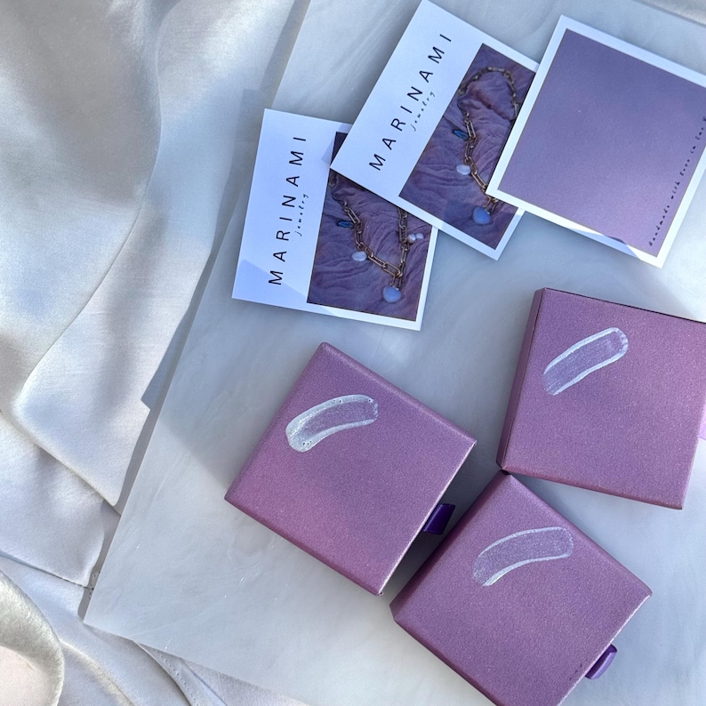purple jewelry boxes with white markings, along with some photographs of jewelry and a white cloth.