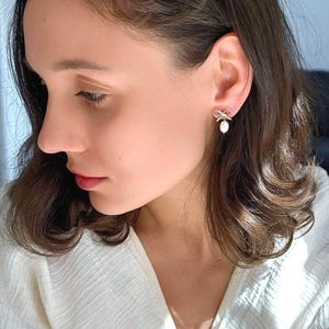 Close-up of a model wearing the earrings, turned in profile. The delicate bow and dangle pearl create an elegant coquette aesthetic for everyday or weddings.