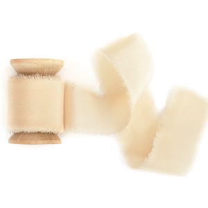 May include: A spool of off-white satin ribbon with a wooden spool. The ribbon is curled and flowing.