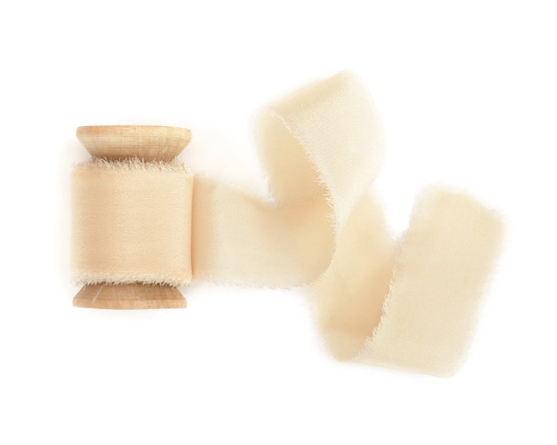 May include: A spool of off-white satin ribbon with a wooden spool. The ribbon is curled and flowing.