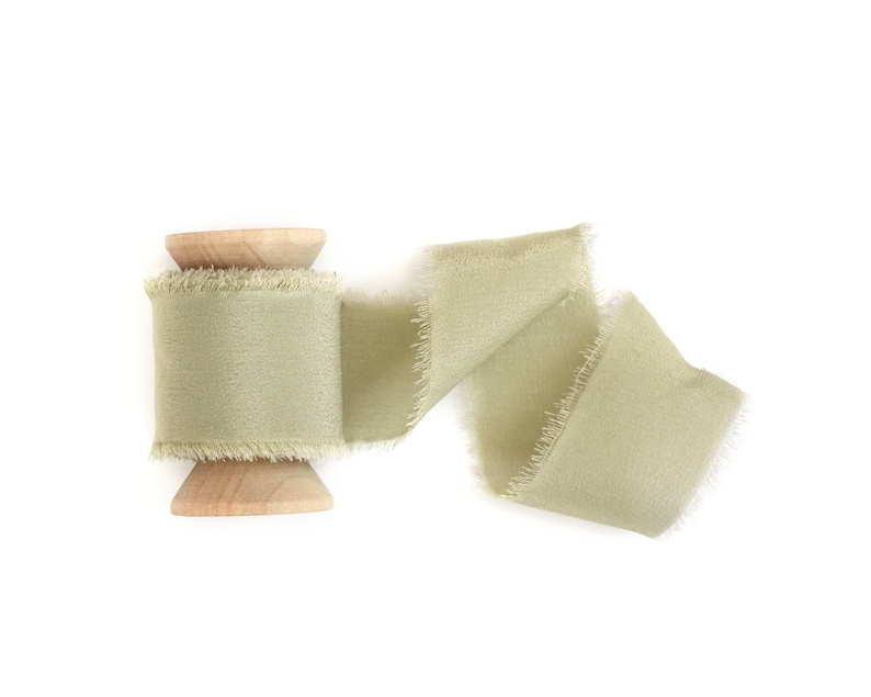 May include: A spool of sage green silk ribbon with frayed edges, wound around a wooden spool.