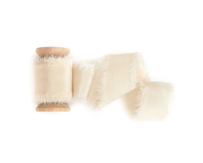 May include: A spool of off-white frayed ribbon with a wooden spool.