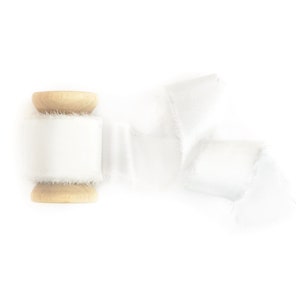 May include: A spool of white satin ribbon with a frayed edge, wrapped around a wooden spool.