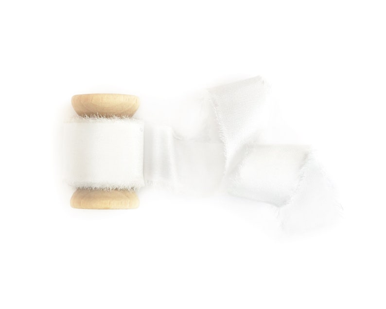 May include: A spool of white satin ribbon with a frayed edge, wrapped around a wooden spool.