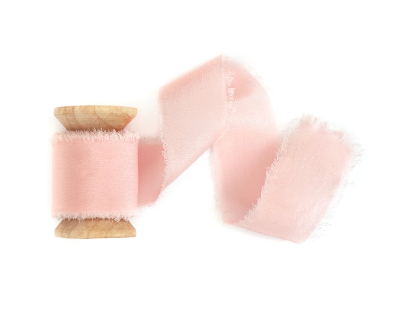 May include: A spool of pale pink ribbon with frayed edges. The ribbon is wound around a wooden spool.