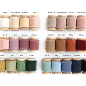 May include: A collection of 20 spools of ribbon in various colors, including ivory, champagne, apricot, peach, rose ash, hazelwood, lotus, flamingo, blush, lilac, grape, mauve, hazelnut, caramel, clay, ruby, pistachio, dew, mint, forest, aqua, sky, provence, indigo, and black. The spools are made of wood and have a frayed edge.