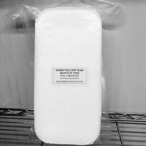 May include: A rectangular block of hard tallow, weighing 5 lbs, encased in clear plastic. The label reads "Hard Tallow 5lbs, Batch # 1002, Pure, Unbleached, Not for Consumption, www.tenderlovingtallow.com". The product is displayed on a wire shelf.