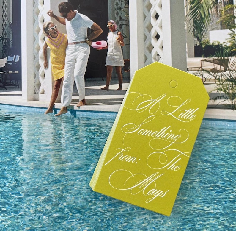 May include: A rectangular chartreuse gift tag with a hole at the top, featuring white cursive text that reads A Little Something From: The Mays, set against a background of a swimming pool with three people standing on the edge of the deck.
