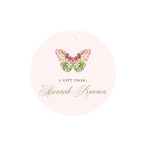 May include: A round pink gift tag with a green and pink butterfly illustration. The text "A gift from, Hannah Rawson" is printed in green cursive font.
