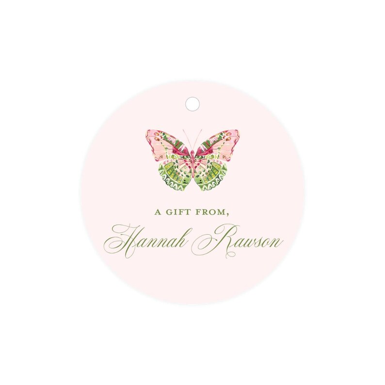 May include: A round pink gift tag with a green and pink butterfly illustration. The text "A gift from, Hannah Rawson" is printed in green cursive font.