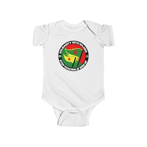 May include: White baby bodysuit with a circular graphic. The graphic features a flag with red, yellow, and green colors, a red star, and the text "SOLIDARITY WITH ROJAVA", "STOP FASCISM", and "RISE UP".