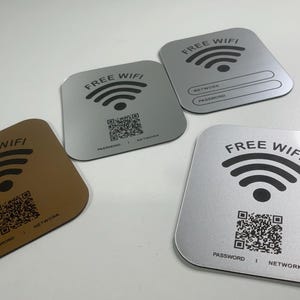 Puede incluir: Cuatro letreros cuadrados con las palabras "FREE WIFI" impresas en ellos. Cada letrero tiene un símbolo de wifi, un código QR y las palabras "PASSWORD" y "NETWORK". Los letreros son de diferentes colores: marrón, plateado y gris.