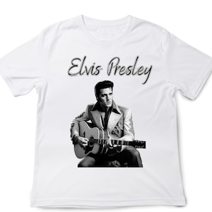 May include: White t-shirt with a black and white image of Elvis Presley playing a guitar. The text "Elvis Presley" is written in cursive above the image.
