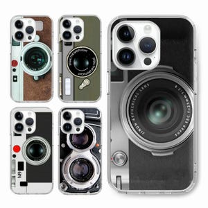 Puede incluir: Cuatro fundas de teléfono diferentes con diseños de cámara. Las fundas son transparentes y muestran los objetivos de la cámara del teléfono. Los diseños incluyen una cámara vintage, una cámara moderna y una cámara con un objetivo que dice "Steal the Spotlight".