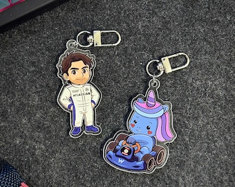 Puede incluir: Dos llaveros acrílicos. Uno presenta un personaje de dibujos animados con un traje de carreras blanco con el texto "ATLASSIAN". El otro es un unicornio azul conduciendo un kart azul. Ambos tienen llaveros plateados.