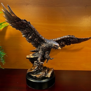 May include: A bronze eagle sculpture with outstretched wings, perched on a rocky base. The eagle has a detailed, realistic appearance with a fierce expression.