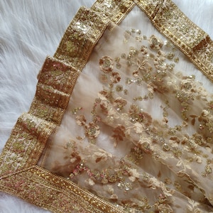May include: A sheer gold and beige embroidered shawl with a gold sequin border. The shawl is made of a delicate fabric and has a floral design.