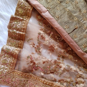 May include: A sheer beige fabric with gold and pink sequins and embroidery. The fabric has a gold border with intricate designs.