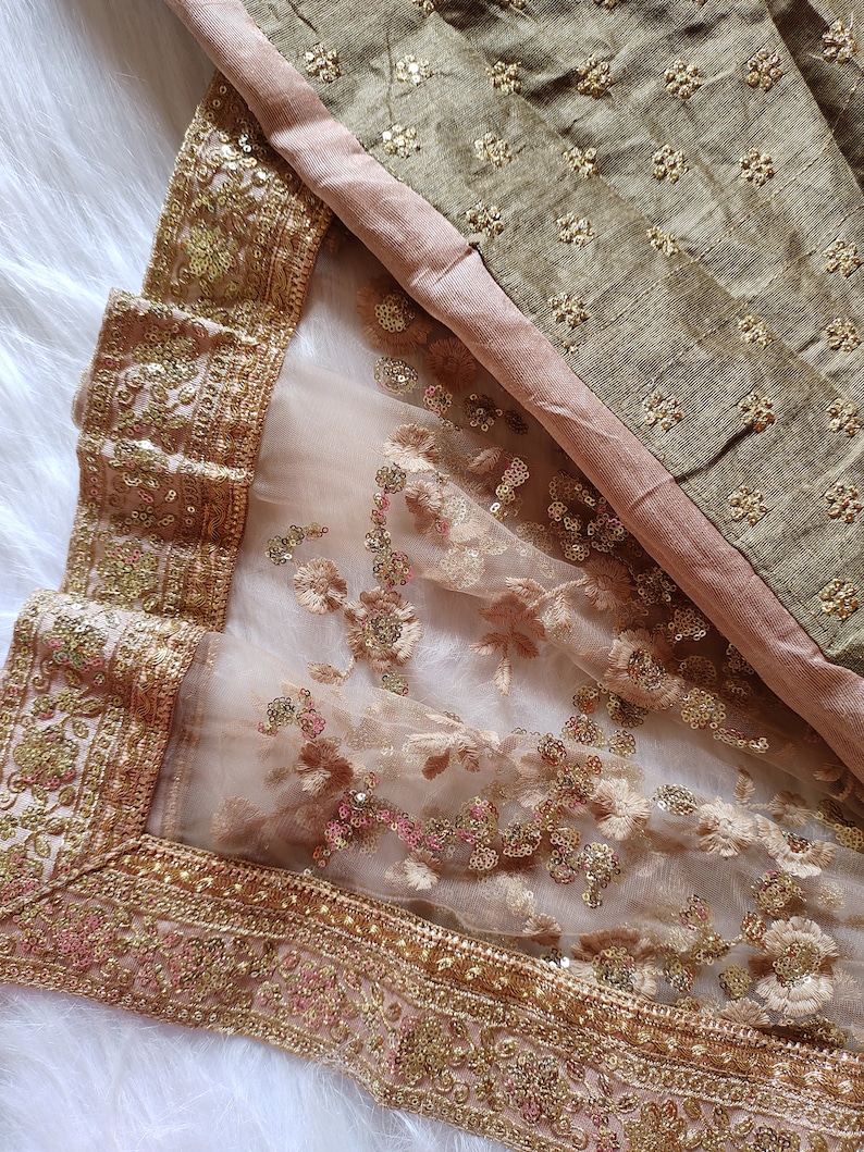 May include: A sheer beige fabric with gold and pink sequins and embroidery. The fabric has a gold border with intricate designs.