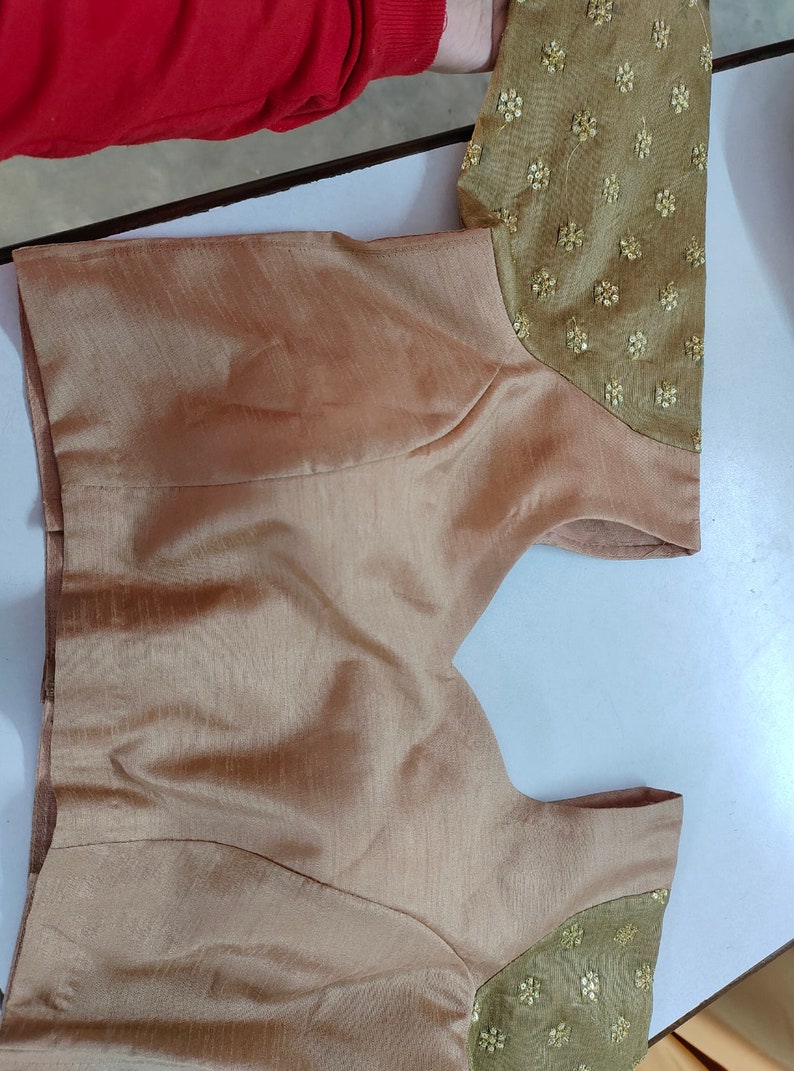 May include: A brown sleeveless blouse with gold embroidered detailing on the sleeves.