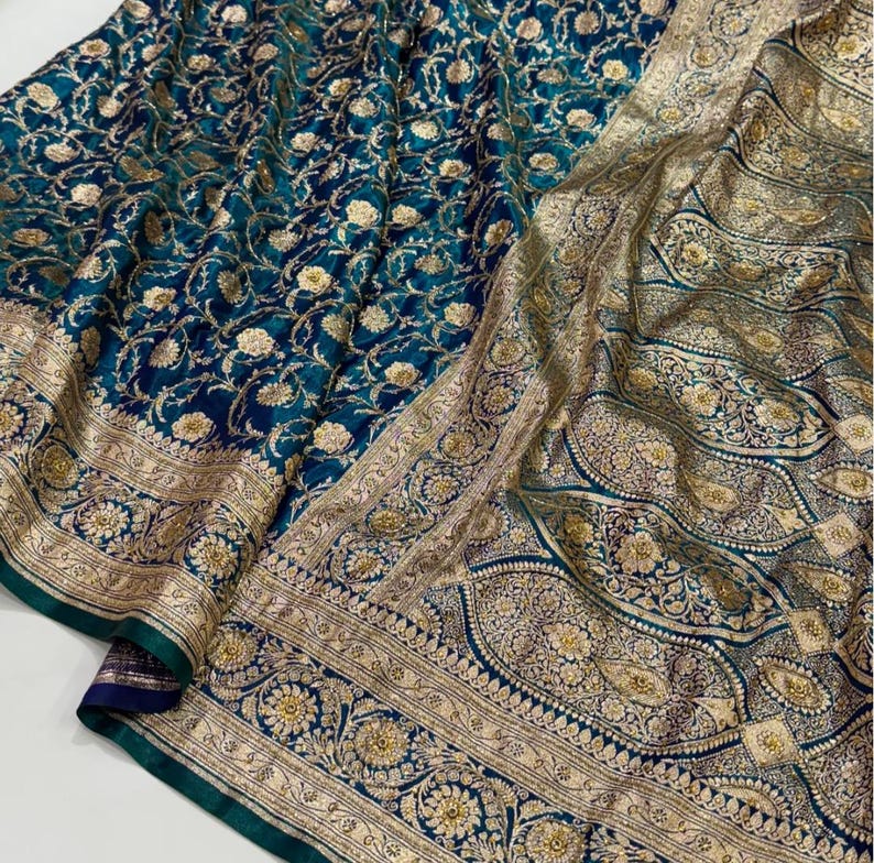 May include: A teal and gold textile with intricate floral patterns. The fabric features a detailed border with gold embellishments. The design includes a combination of floral and paisley motifs, creating a luxurious and ornate appearance.