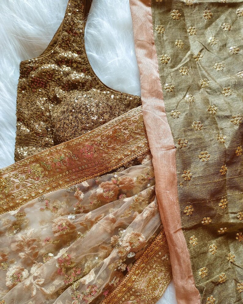 May include: A gold and brown embroidered fabric with sequins. The fabric is sheer and has a delicate floral pattern. The fabric is folded in half and the edges are visible.