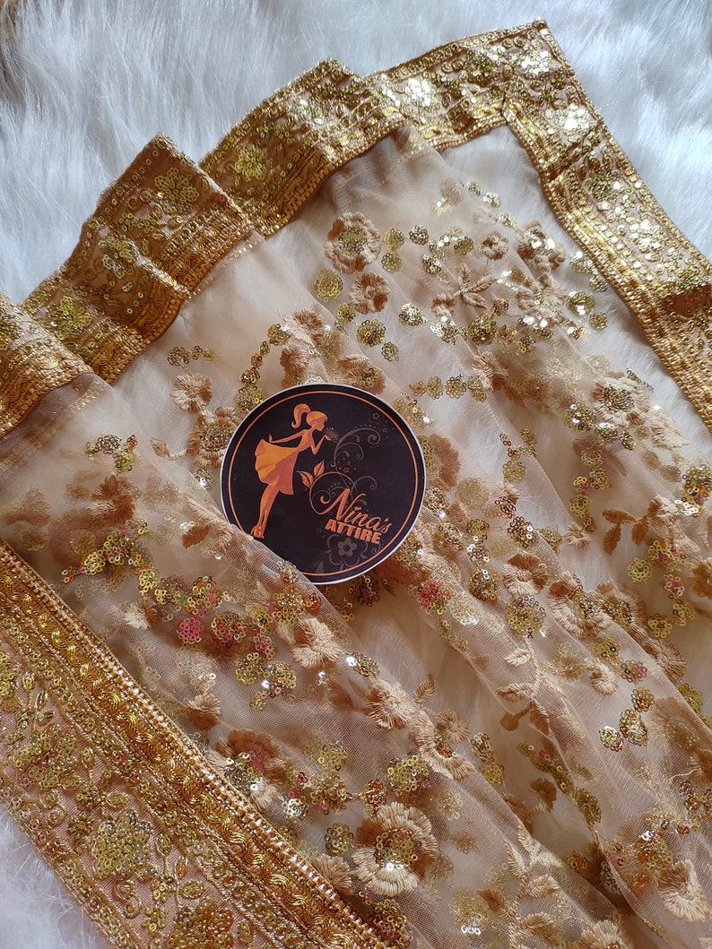 May include: A sheer gold net dupatta with a gold embroidered border and sequins. The dupatta has a floral design and is perfect for a special occasion.