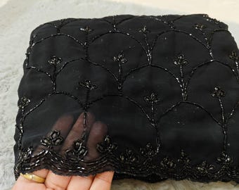 May include: Black sheer fabric with a beaded design of small flowers and arches. The fabric has a scalloped edge.