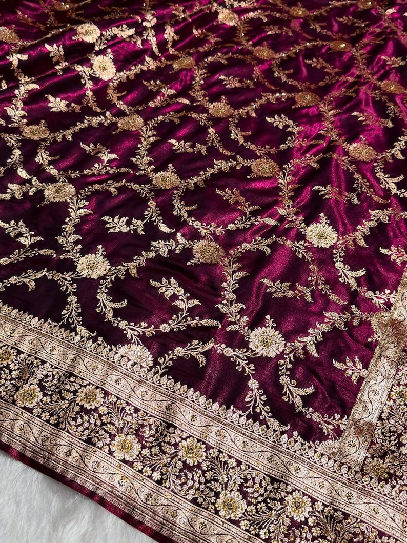 May include: A luxurious, deep burgundy fabric with intricate gold floral embroidery. The design features detailed vines and flowers, with a decorative border along the edge. The fabric has a rich, velvety texture.
