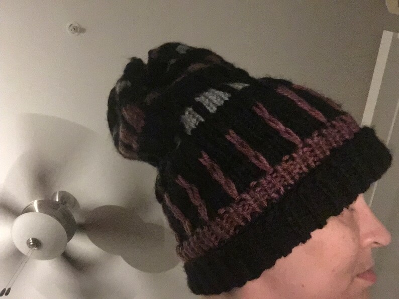 May include: A black knit beanie with pink and gray stripes. The beanie has a pompom on top.