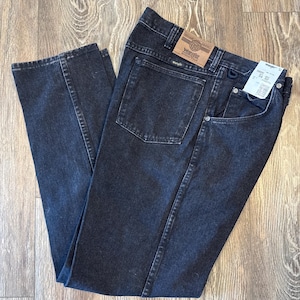 Puede incluir: Un par de pantalones vaqueros negros de denim con una etiqueta Wrangler de cuero marr&oacute;n en el bolsillo trasero. Los vaqueros tienen un corte recto y un dise&ntilde;o cl&aacute;sico de cinco bolsillos.