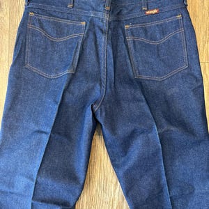 May include: A pair of dark blue denim jeans with a Wrangler label on the back pocket.
