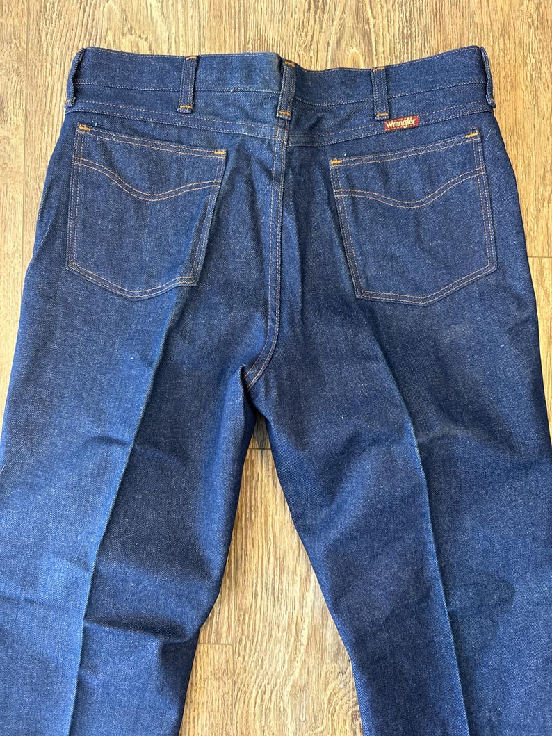 May include: A pair of dark blue denim jeans with a Wrangler label on the back pocket.