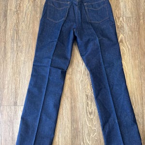 May include: A pair of dark blue denim jeans with a straight leg fit. The jeans have a classic five-pocket design and a button fly.