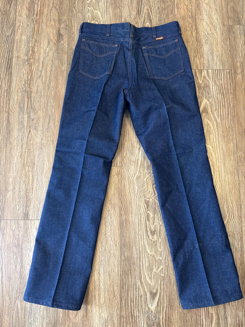 May include: A pair of dark blue denim jeans with a straight leg fit. The jeans have a classic five-pocket design and a button fly.