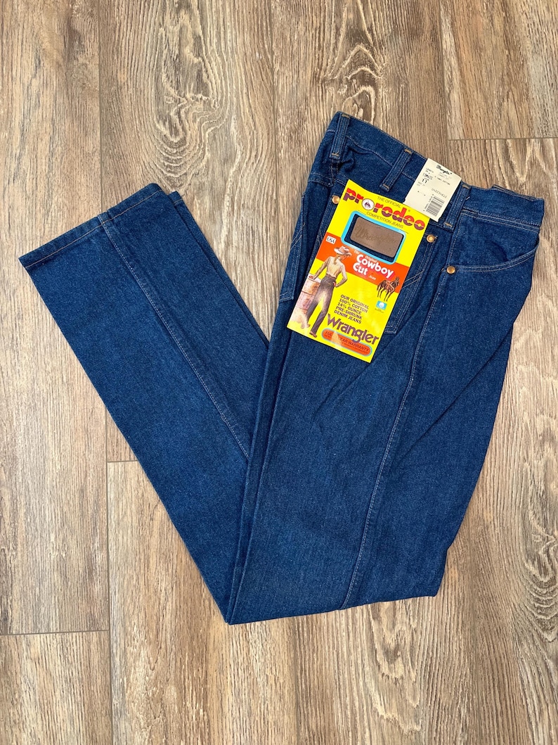May include: A pair of dark blue denim jeans with a Wrangler ProRodeo Cowboy Cut label attached. The label features a woman wearing the jeans and the text "ProRodeo Cowboy Cut" and "Wrangler".
