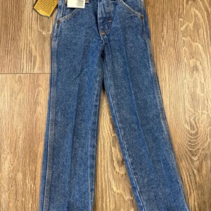 Puede incluir: Un par de pantalones vaqueros azules de mezclilla con cierre de bot&oacute;n y cinco bolsillos. Los pantalones tienen una etiqueta de Wrangler en el bolsillo trasero.