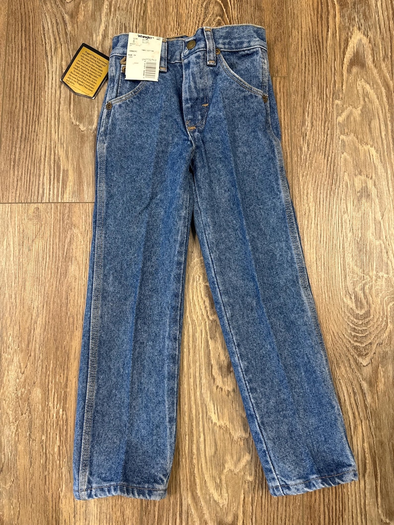 Puede incluir: Un par de pantalones vaqueros azules de mezclilla con cierre de bot&oacute;n y cinco bolsillos. Los pantalones tienen una etiqueta de Wrangler en el bolsillo trasero.