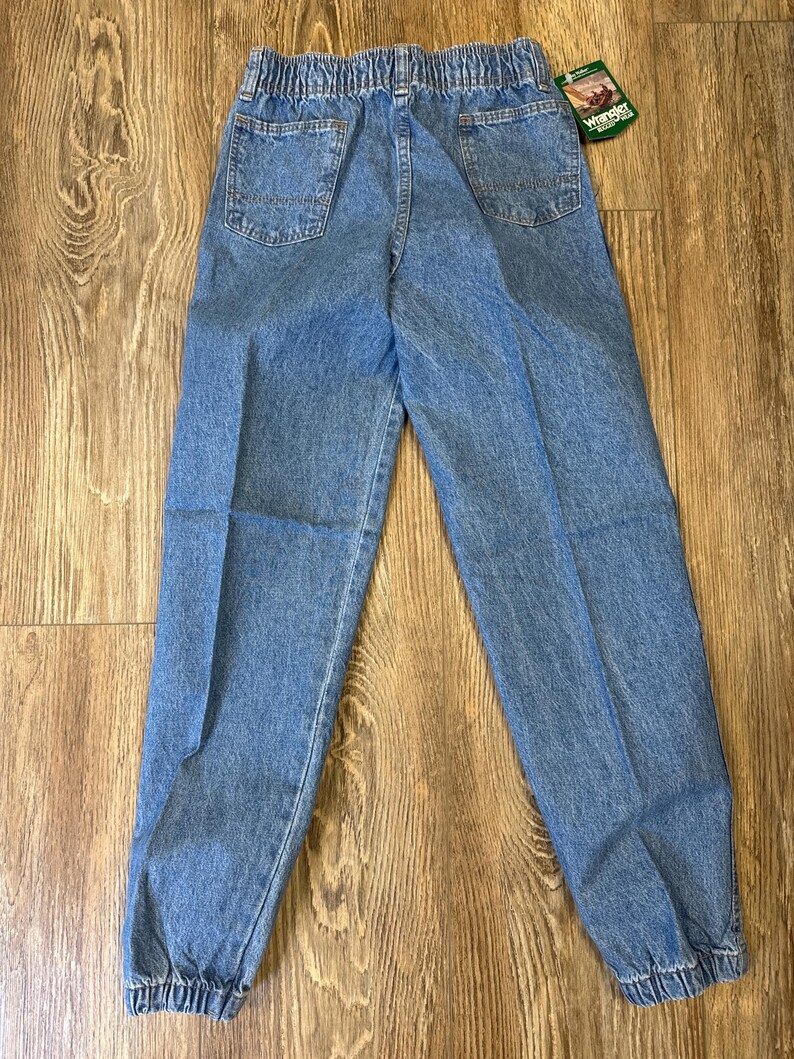 K&ouml;nnte beinhalten: Hellblaue Jeanshose mit elastischem Bund und elastischen B&uuml;ndchen. Die Hose hat zwei Ges&auml;&szlig;taschen und ein Etikett mit der Aufschrift "Wrangler". Hergestellt aus strapazierf&auml;higem Denim.