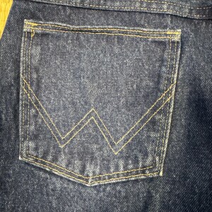 K&ouml;nnte beinhalten: Nahaufnahme einer dunkelblauen Jeans-Tasche mit gelber Naht. Die Tasche hat ein markantes gelbes "W"-Design. Der Denim hat eine strukturierte Optik.