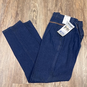 Puede incluir: Un par de pantalones vaqueros de mezclilla azul oscuro con un ribete de cuero marr&oacute;n en la cintura. Los pantalones tienen una etiqueta de Wrangler en el bolsillo trasero y una etiqueta de Wrangler m&aacute;s peque&ntilde;a en la parte delantera.