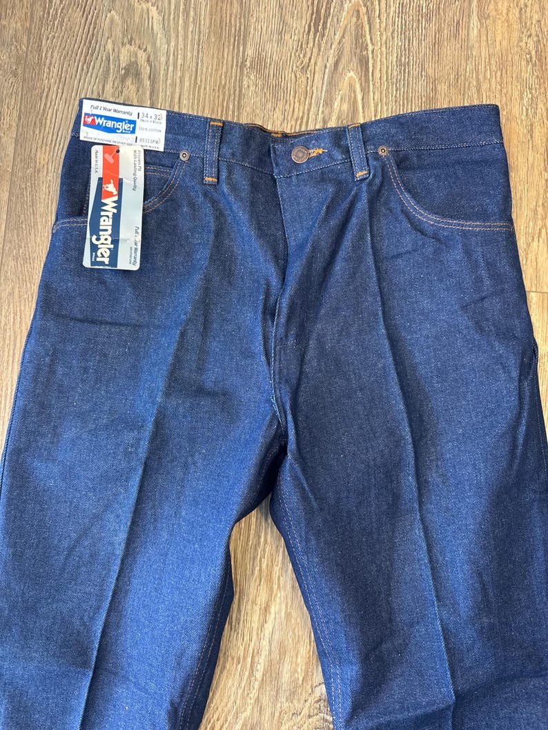 May include: A pair of blue denim jeans with a Wrangler tag attached. The tag says "Full Year Warranty" and "Wrangler" with the size "34 x 32".
