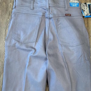 May include: Light blue Wrangler Flex Fit waist jeans. The back view shows the pockets, belt loops, and the Wrangler logo. The tag reads "FLEX-FIT WAIST" for added comfort. The jeans are made of a durable fabric.