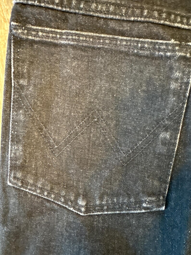 Puede incluir: Primer plano de un bolsillo de mezclilla negro con un patr&oacute;n de costura distintivo. El bolsillo est&aacute; desgastado y deste&ntilde;ido, lo que le da un aspecto vintage.