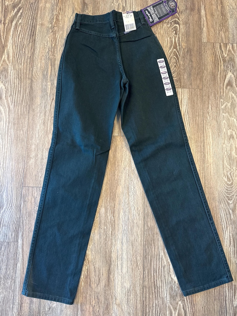 May include: Dark green straight leg jeans with a purple and white tag that says "Wrangler Rugged Wear" and "Made in the USA".